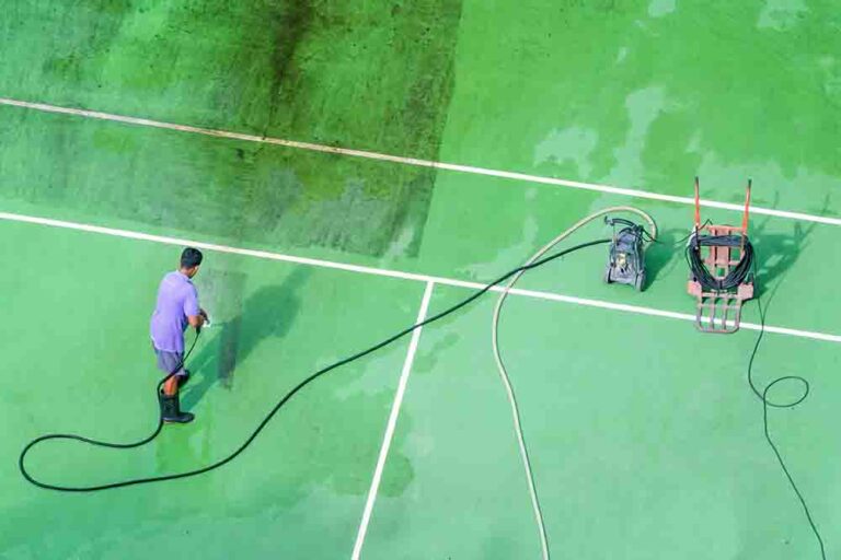 Pressure Cleaning Tennis Court half is clean half is dirty. There's a man cleaning the tennis court with a pressure washer