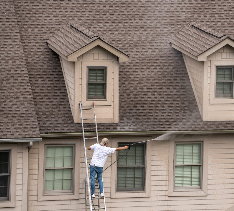 Man standing on a ladder pressure cleaning the exterior of a house