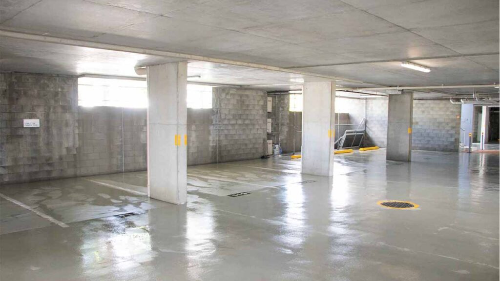 Photo showing a freshly pressure cleaned commercial car park. 5 car parks can been seen, the roof and floor are made from concrete with a brick wall.