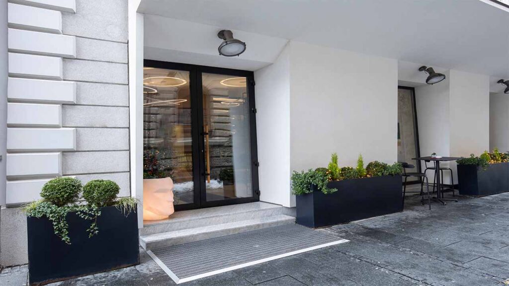 Hotel front that has just been pressure cleaned. The photo is looking at the entry which is a double glass door, the building is white with rectangular plant boxes spaced along the front.