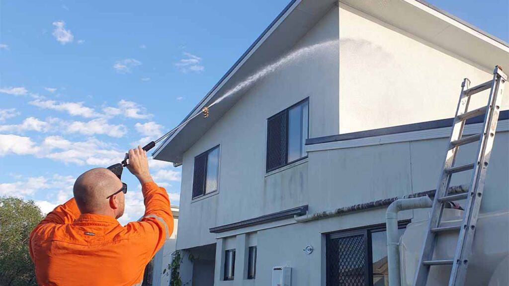 Member of Pressure Washed South East Qld washing a white two story house with a pressure washer.