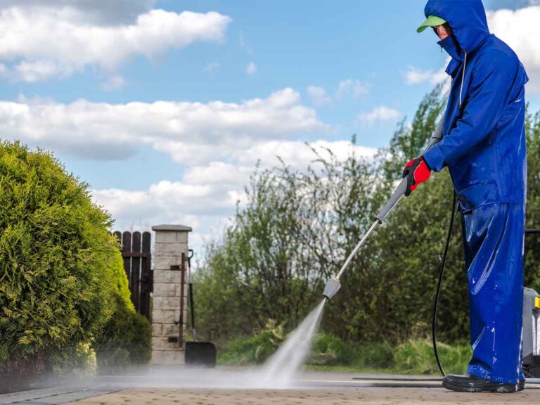Man dressed in a blue water proof suit using a high pressure washer to clean a concrete surface