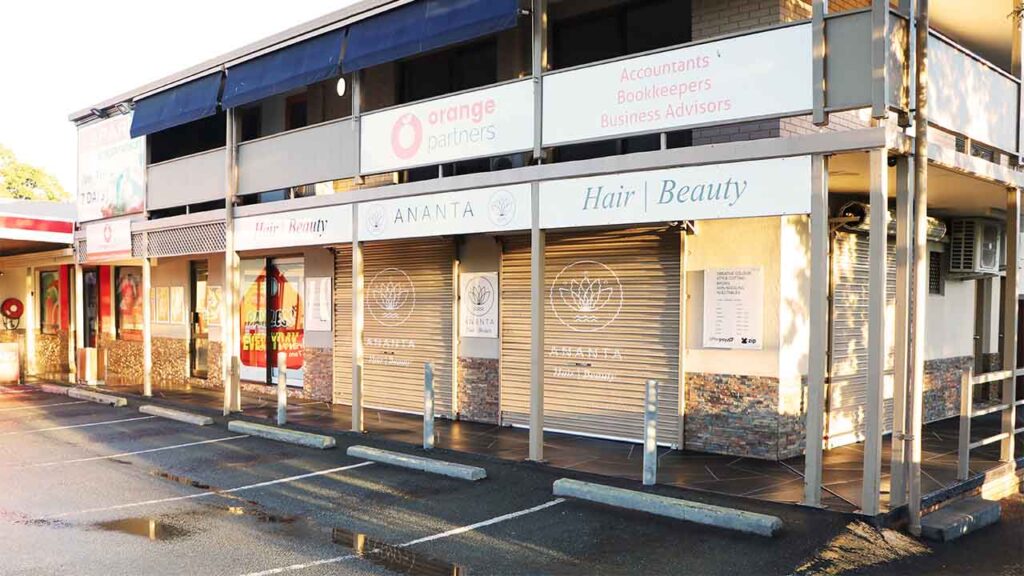 Photo of a shop front that has just been pressure washed. It's a two story building that has signs for the shops displayed on the second level. Park of the car park is visible in the photo and is still wet from the pressure cleaning