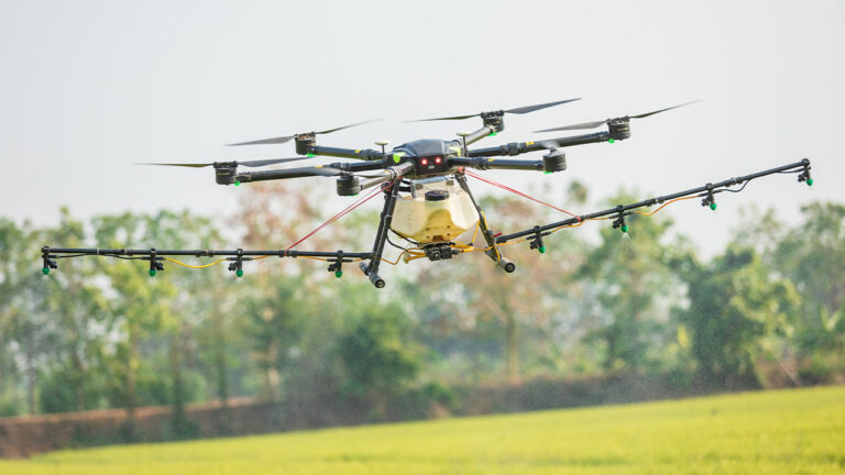 A large commercial drone with pressure sprayer attached. Flying over a field with tree's in the background