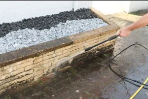 Power washing a white colored brick wall that is covered in organic growth
