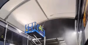 Photo of a team member using a sizzor lift to pressure clean the underneath of a dirty shade sail. It's night time and water mist can be seen in the air from the pressure washer.