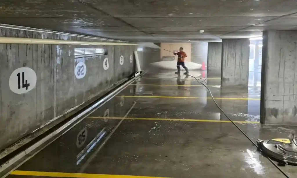 Photo of a team member of Pressure Washed South East QLD pressure cleaning the wall of an underground concrete car park. The water on the concrete floor is reflecting the roof.