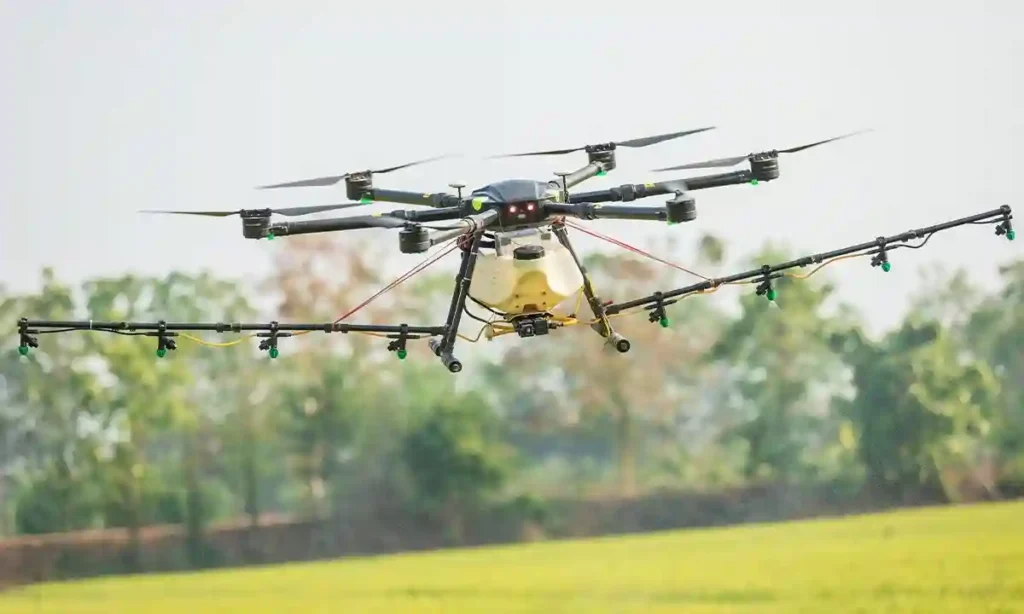 Photo of a large commercial drone spraying a field. The drone has 6 rotors and a large spray bay connected to the bottom of the drone.